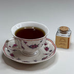 Tea cup with floral design on a saucer next to a small bottle of tea leaves on a gray background
