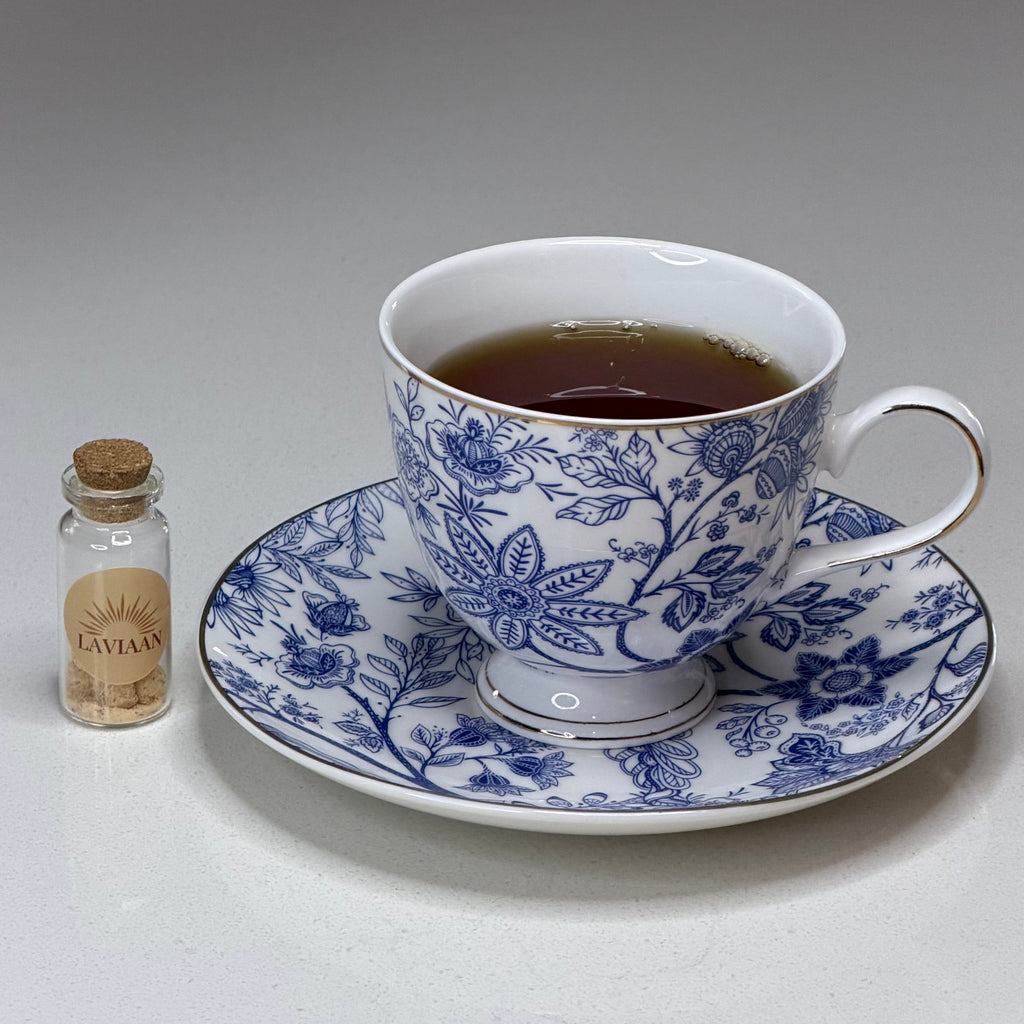 Teacup with floral design on a saucer, accompanied by a small bottle of tea leaves on a gray background