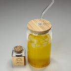 Glass jar with wooden lid and straw, next to a small bottle on a gray background