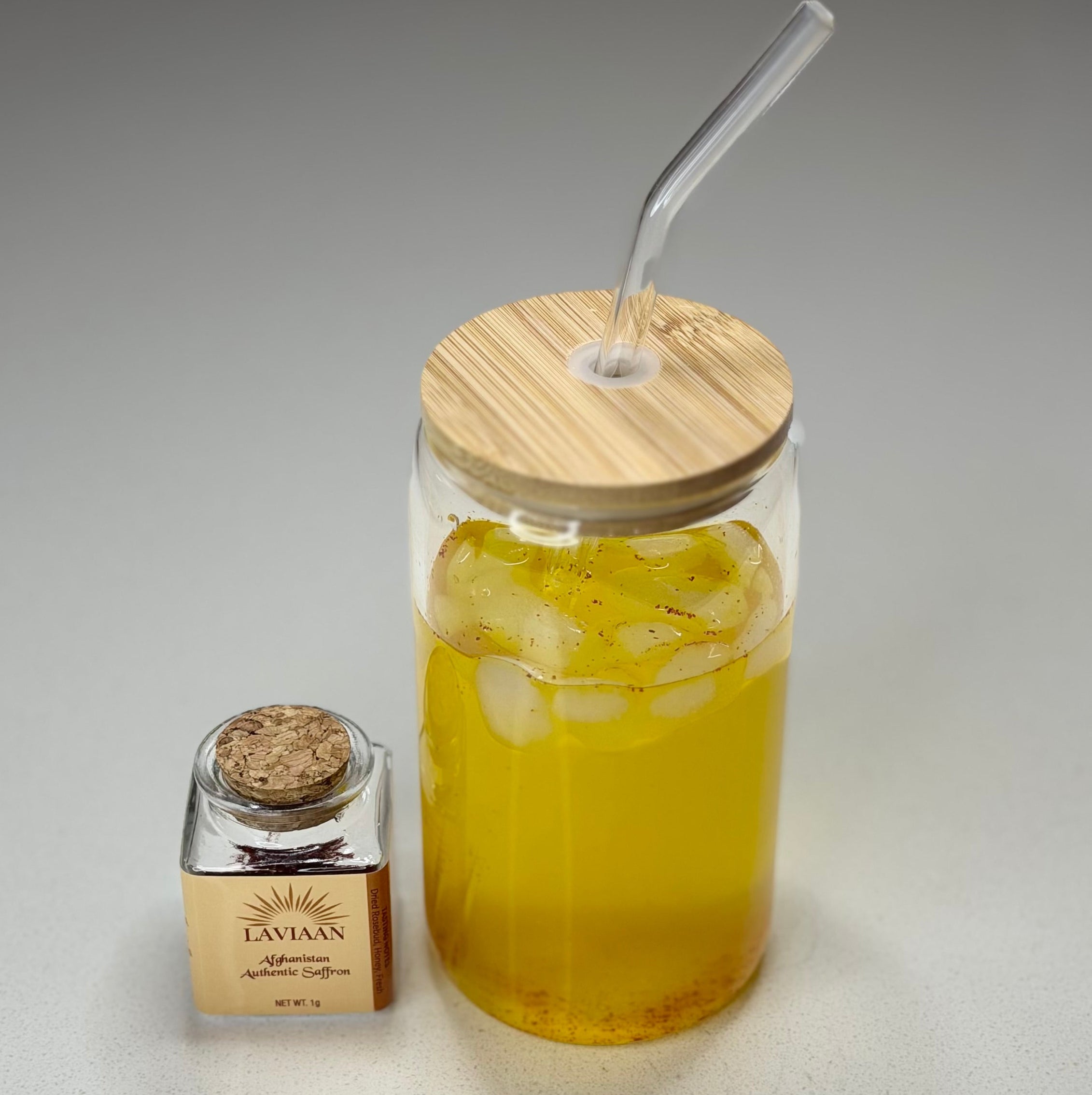 Glass jar with wooden lid and straw, next to a small bottle on a gray background