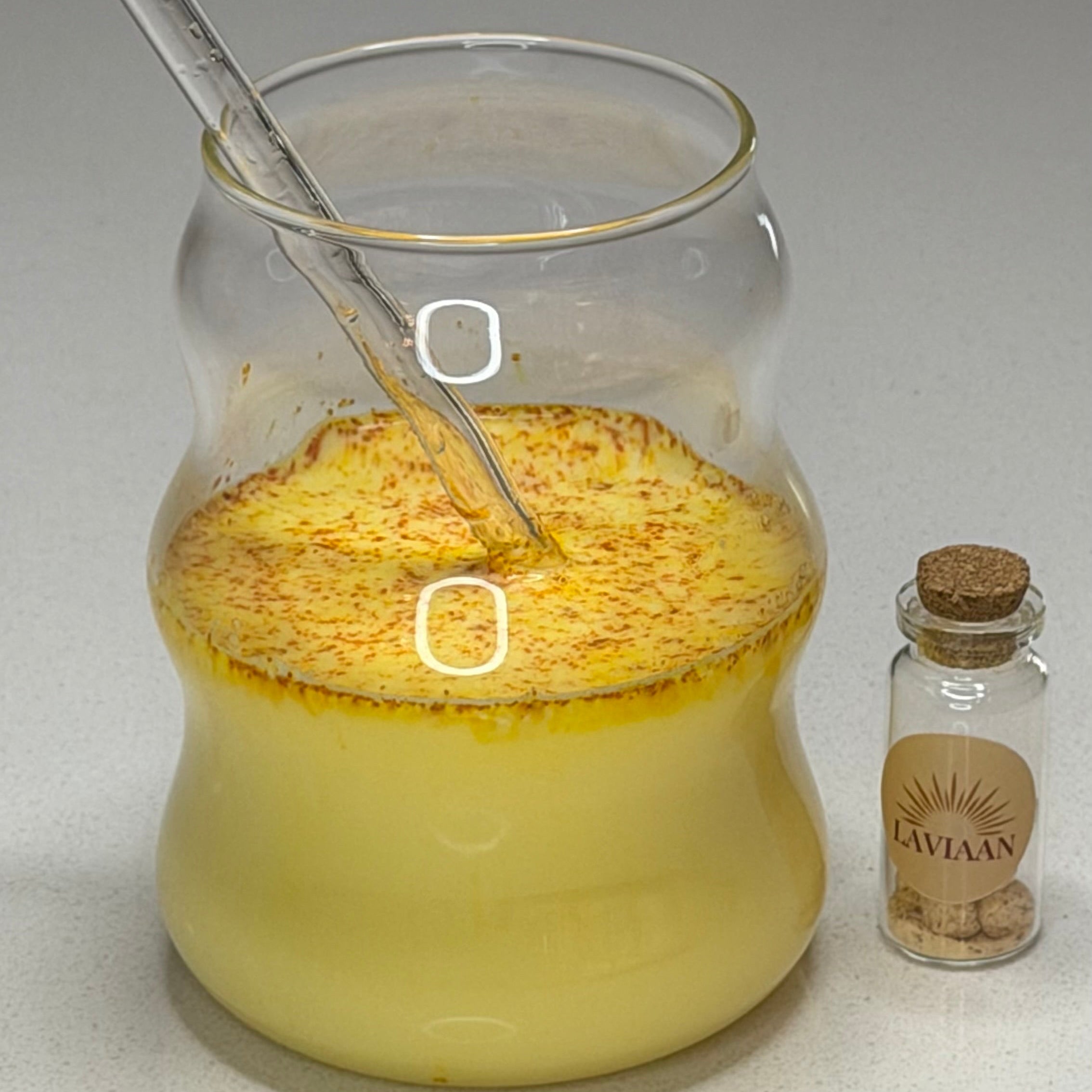 Glass jar with yellow powder and liquid, corked bottle labeled 'Bakvar' on a white surface.